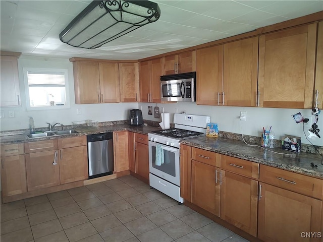 kitchen featuring stainless steel appliances, dark stone counters, brown cabinetry, and a sink