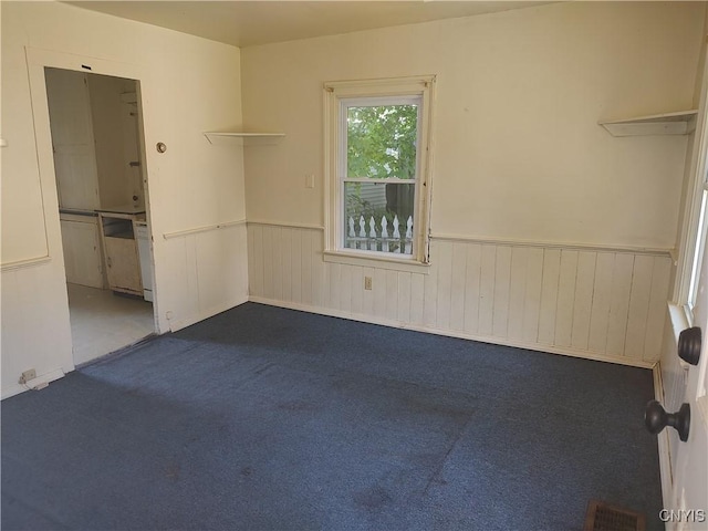 carpeted spare room with visible vents and wainscoting