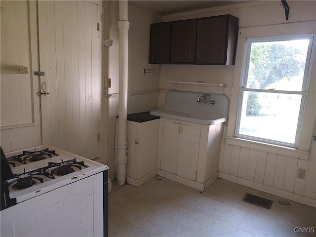 kitchen featuring a healthy amount of sunlight, light floors, white range with gas stovetop, and a sink