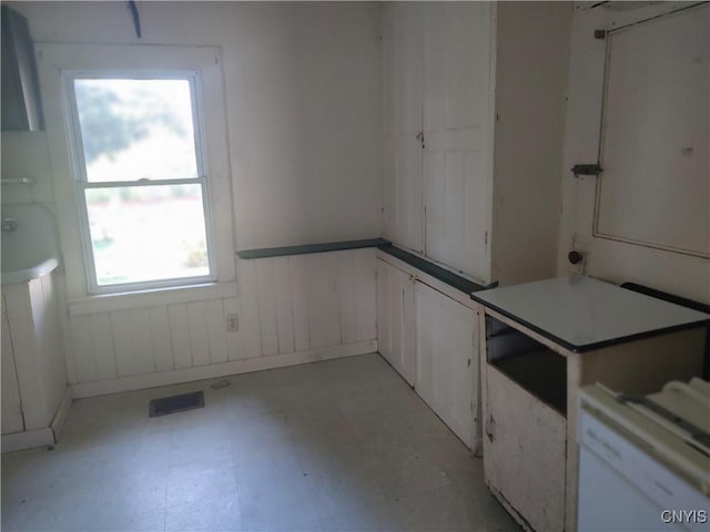 kitchen with a wainscoted wall, light floors, visible vents, and white cabinets