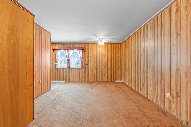 unfurnished room featuring carpet floors, wooden walls, and a ceiling fan