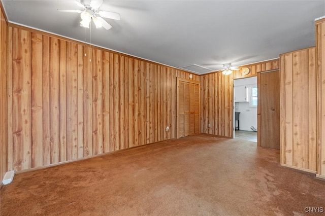 unfurnished room with wood walls, carpet, attic access, and a ceiling fan