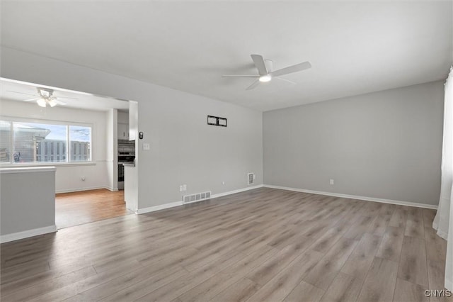 unfurnished room with light wood-style floors, ceiling fan, visible vents, and baseboards