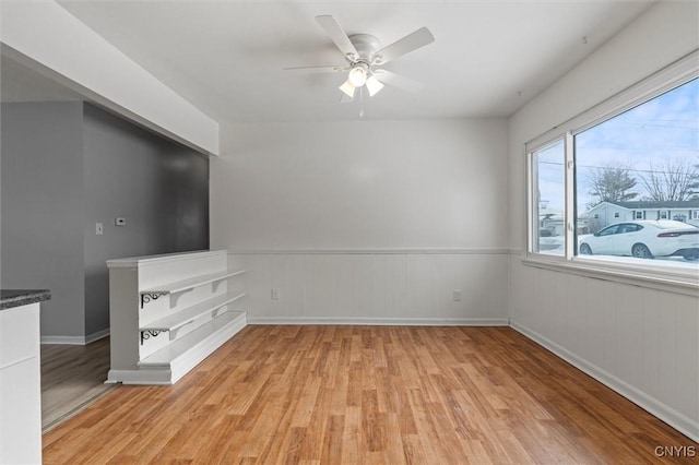 unfurnished living room featuring a wainscoted wall, ceiling fan, and light wood finished floors