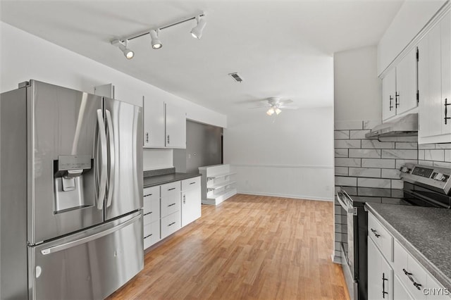 kitchen with under cabinet range hood, appliances with stainless steel finishes, backsplash, light wood finished floors, and dark countertops