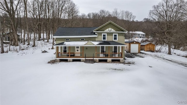 snow covered back of property with a garage, covered porch, and an outdoor structure