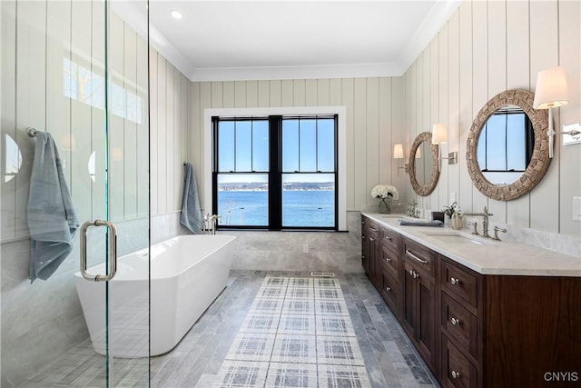 bathroom with a freestanding tub, a sink, ornamental molding, double vanity, and a stall shower