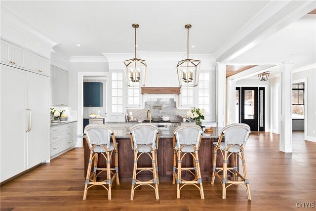 kitchen featuring paneled fridge, a kitchen breakfast bar, backsplash, decorative columns, and crown molding