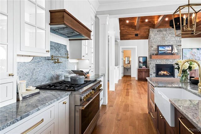 kitchen with light wood-style flooring, stainless steel stove, a sink, decorative backsplash, and custom range hood