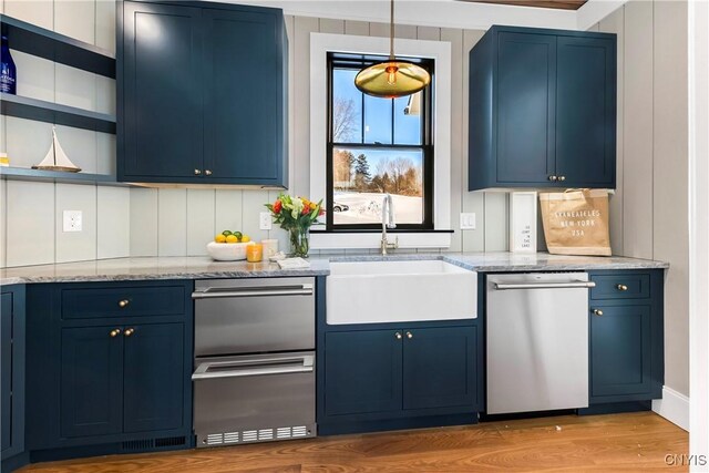 kitchen with blue cabinets, a sink, light stone countertops, dishwasher, and open shelves