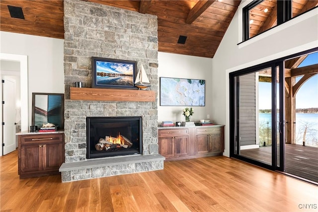 living area with wood ceiling, light wood-style flooring, beamed ceiling, and a stone fireplace