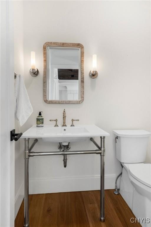 half bath featuring toilet, a sink, baseboards, and wood finished floors