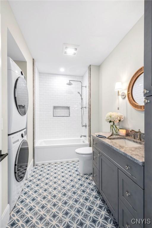 bathroom featuring toilet, shower / bathing tub combination, stacked washing maching and dryer, and vanity