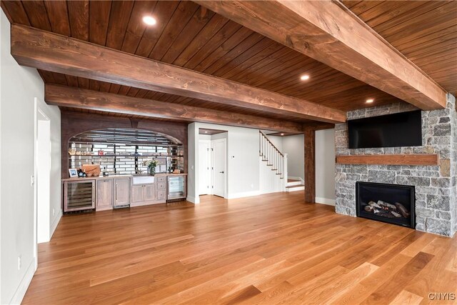 unfurnished living room featuring a stone fireplace, beverage cooler, wood finished floors, stairway, and a bar