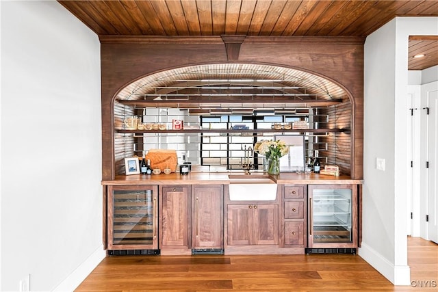 bar with light wood-style floors, wine cooler, wooden ceiling, and wet bar