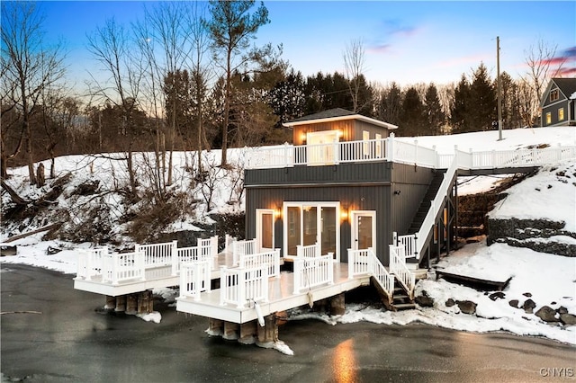 snow covered back of property featuring a deck and stairway