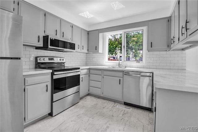 kitchen with marble finish floor, light countertops, gray cabinetry, appliances with stainless steel finishes, and a sink