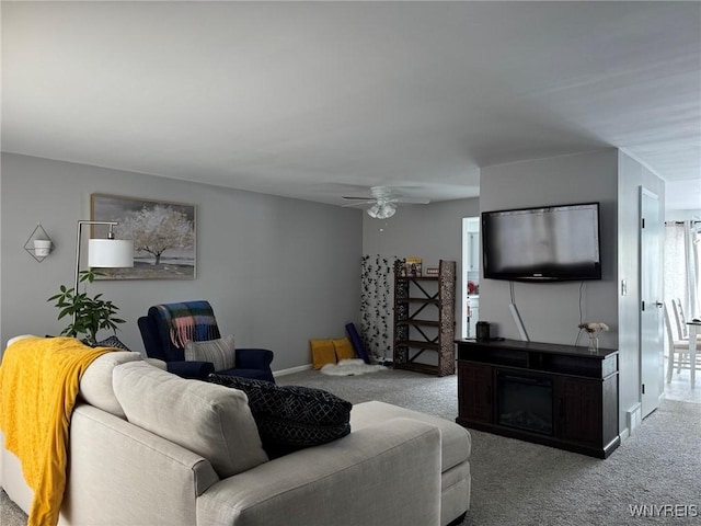 carpeted living room with a ceiling fan, a fireplace, and baseboards