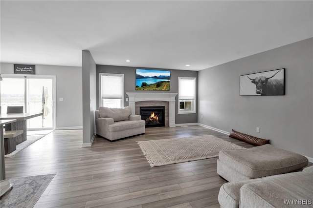 living room featuring recessed lighting, a warm lit fireplace, baseboards, and wood finished floors