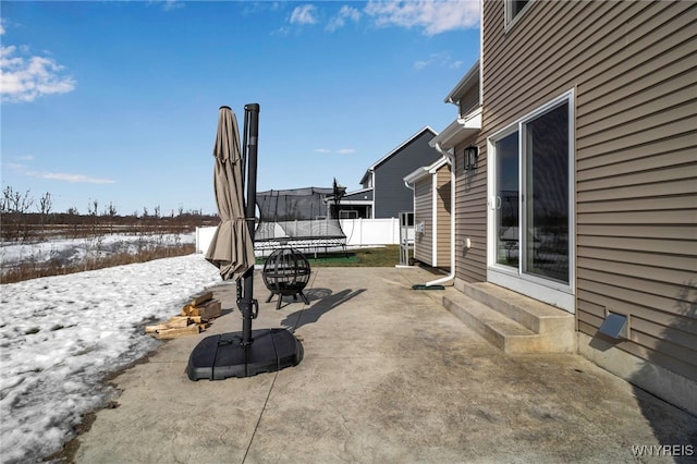 snow covered patio with a trampoline, entry steps, and fence