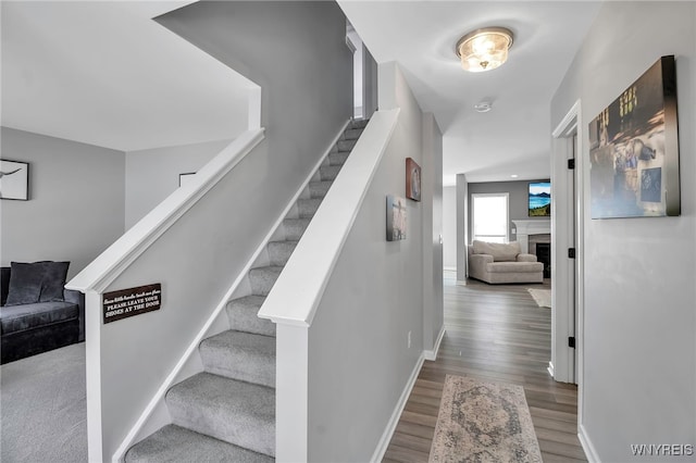 staircase featuring a fireplace, baseboards, and wood finished floors