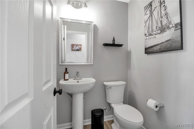 half bath with toilet, baseboards, and a sink