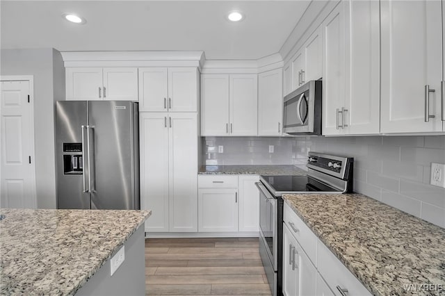 kitchen with light stone counters, decorative backsplash, appliances with stainless steel finishes, white cabinetry, and light wood-type flooring