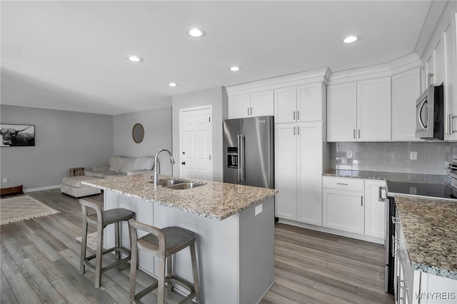 kitchen with stainless steel appliances, backsplash, open floor plan, white cabinetry, and a sink