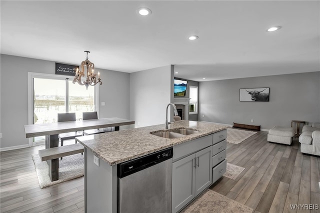 kitchen featuring a fireplace, stainless steel dishwasher, open floor plan, a sink, and wood finished floors