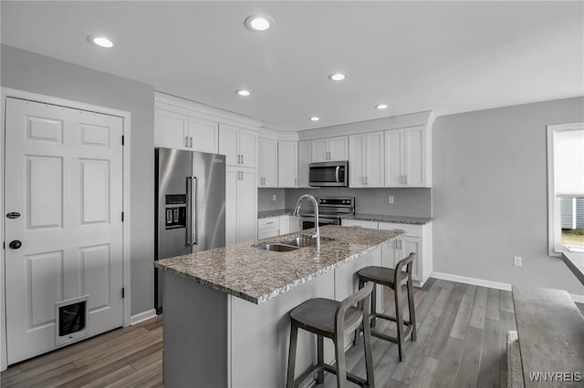 kitchen with appliances with stainless steel finishes, white cabinets, a sink, and wood finished floors