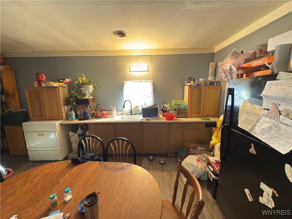 kitchen with wood finished floors, visible vents, a sink, freestanding refrigerator, and brown cabinetry