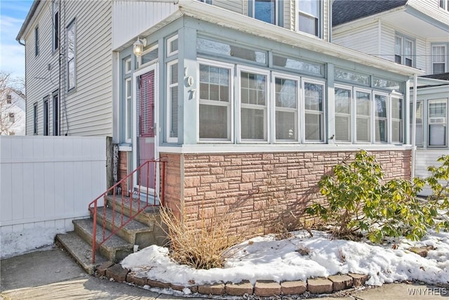 view of home's exterior featuring stone siding, a sunroom, and fence