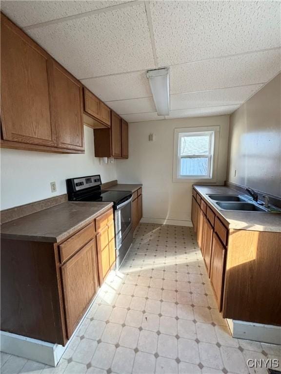 kitchen featuring a drop ceiling, light floors, brown cabinets, electric stove, and a sink