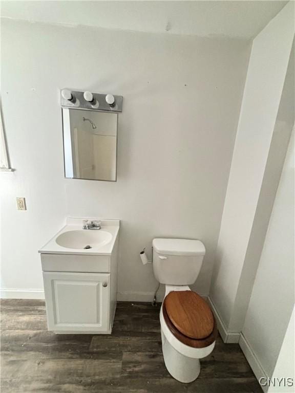 half bath featuring vanity, toilet, wood finished floors, and baseboards