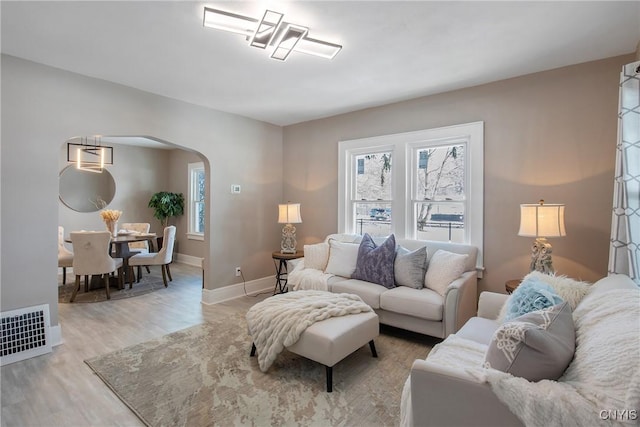 living room featuring visible vents, arched walkways, light wood-style flooring, and baseboards