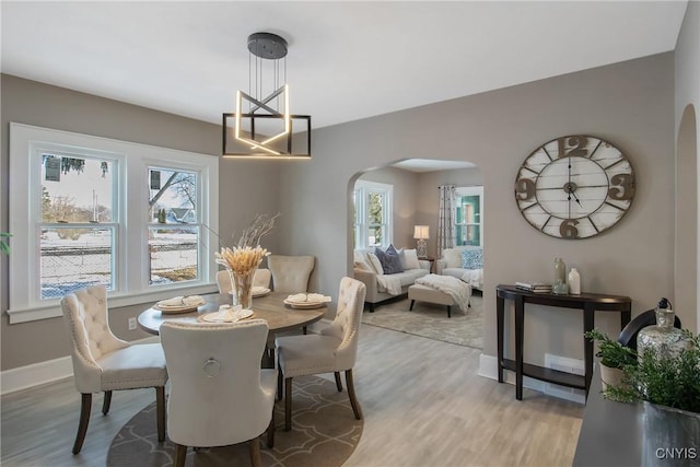 dining space featuring light wood-style floors, arched walkways, a healthy amount of sunlight, and baseboards