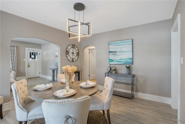 dining room with light wood-type flooring, baseboards, and arched walkways