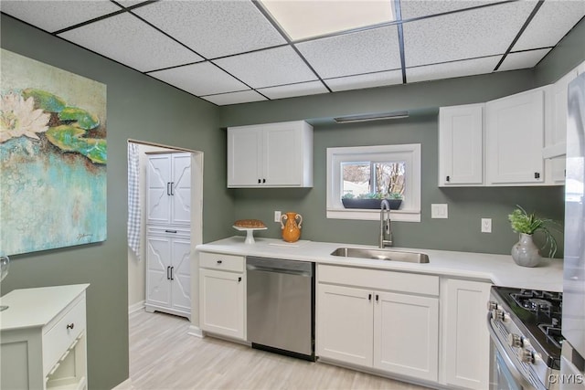 kitchen with a sink, light wood-style floors, white cabinets, light countertops, and appliances with stainless steel finishes