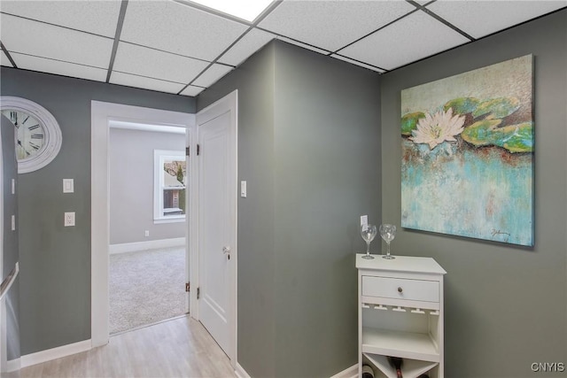 corridor featuring a paneled ceiling, baseboards, and wood finished floors