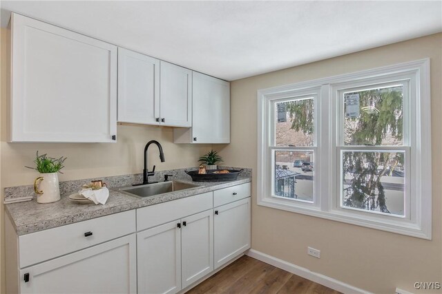 kitchen with wood finished floors, a sink, white cabinetry, baseboards, and light countertops