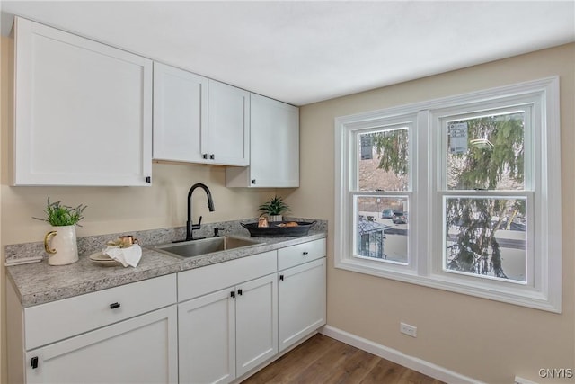 kitchen featuring wood finished floors, a sink, baseboards, white cabinets, and light countertops