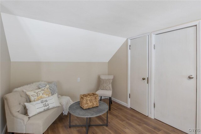 living area with vaulted ceiling, baseboards, and wood finished floors