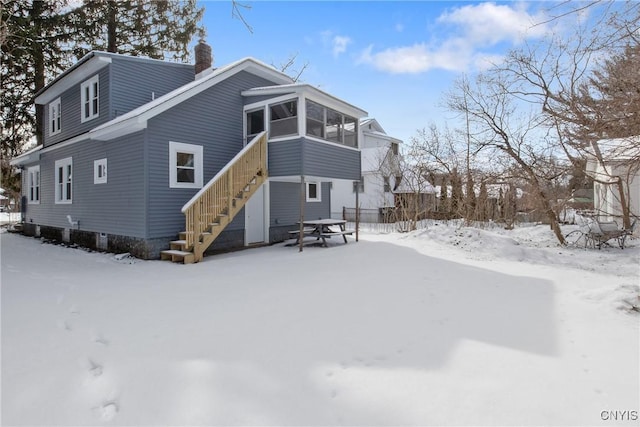 snow covered property featuring a sunroom, stairs, and a chimney