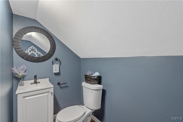bathroom with vaulted ceiling, a textured ceiling, vanity, and toilet