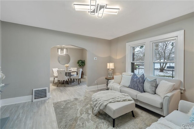 living room featuring arched walkways, wood finished floors, visible vents, and baseboards