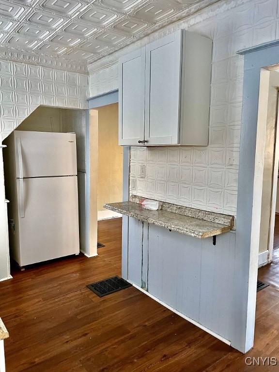 kitchen featuring visible vents, an ornate ceiling, light stone counters, dark wood-style flooring, and freestanding refrigerator