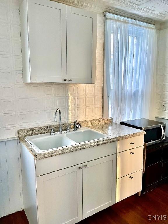 kitchen with dark wood-style floors, light countertops, backsplash, white cabinetry, and a sink