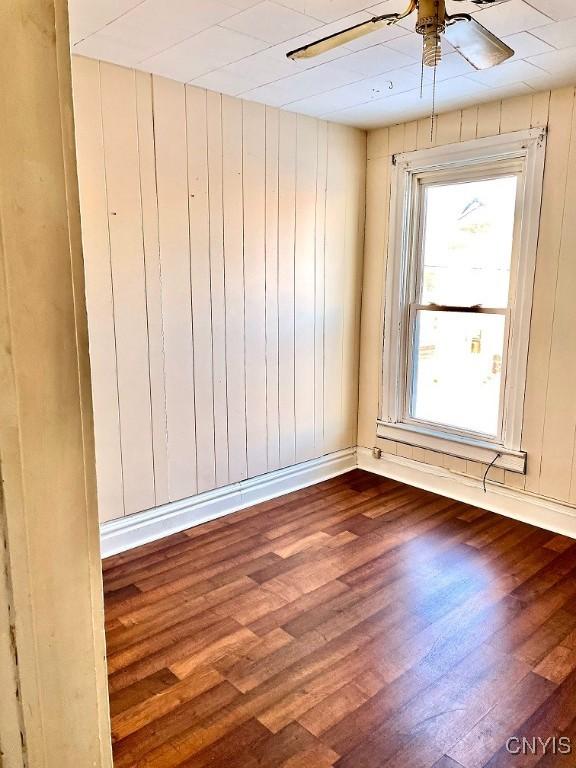 spare room with dark wood-type flooring, ceiling fan, and wooden walls