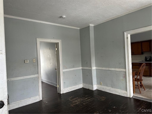 empty room with crown molding, a textured ceiling, baseboards, and wood finished floors