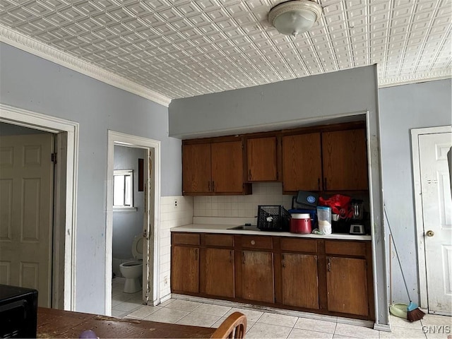 kitchen with light tile patterned floors, brown cabinetry, an ornate ceiling, light countertops, and backsplash